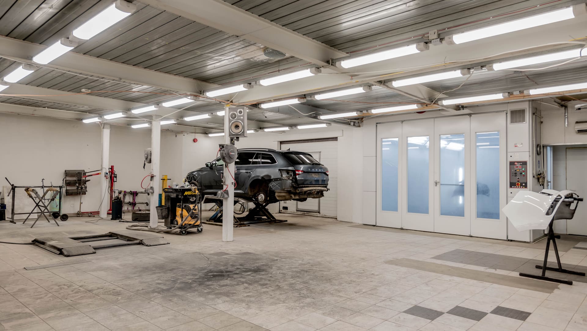 Panel repair workshop with a car raised on a lift and a spray booth on the right
